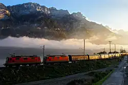 Die beiden Re 4/4 II Loks 11313 und 11293 im Streiflicht,kommen wenige Sekunden nach Sonnenaufgang mit einem im Morgenlicht golden aufglänzenden Ganzzug aus Schiebewandwagen bestehend,bei