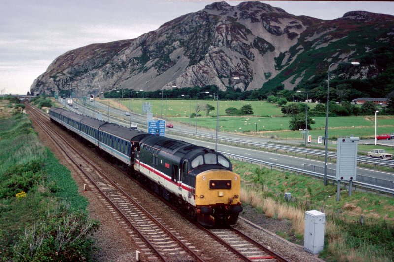 Wegen fehlender Dieseltriebwagen gab es zwischen 1994 und 2000 diesellok bespannte Regionalzuege auf der Strecke Crewe-Holyhead entlang der Nord Wales Kueste. Am 18. August 1994 zieht 37407 eine Manchester-Holyhead Regionalzug westlich von Abergelly.