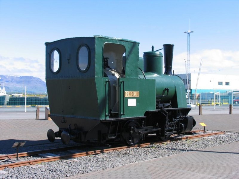 You can find this locomotive (Minr) in the harbour of the capital Reykjavik. Iceland's first (one of three) railway, the Reykjavik Harbour Railway, was built to transport  materials to construct the quay and breakwater between the mainland and rfirisey Island. One section of the 90 cm gauge track ran from skjuhli and the other went to Sklavruholt. Two steam locomotives, Pionr and Minr, were purchased from Denmark and transported to Reykjavik. Each locomotive was 3 m high, 49 m long, and weighed 13 tons.  From 1913-1917 the locomotives were quite busy, often making up to 25 trips each day. Even after 1917, the locomotives remained in limited use up to 1928. Interestingly, both locomotives have been preserved. Locomotive Minr is in the harbour of Reykjavik and the locomotive Pionr can be seen at the rbaer open-air museum.