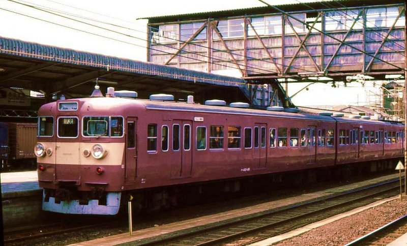 ZWEISTROMZUEGE: Diese haben die Nummerngruppen 400/500/600 ff. Gebiete ausserhalb der Grossagglomerationen wurden grossenteils mit Wechselstrom (erstmals 1961 Strecken in Nordost-Japan, mit 20kV/50Hz) elektrifiziert. Um Anbindung an die grossen Städte zu ermöglichen, waren alle Züge für Wechselstromstrecken (ausser auf Hokkaido) in Zweistromausführung, erstmals Serie 401 (gebaut 1961-1966). Da längere Strecken befahren wurden, haben sie Quersitze und nur 3 statt 4 Seitentüren. Anstrich aller Zweistromzüge urspr. rosa. Hier ist ein Zug mit Steuerwagen KUHA 401-46 in Oyama, 3.Mai 1977.  